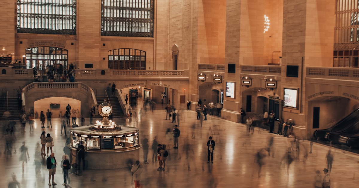 People walking through a grand, ornate train station lobby.