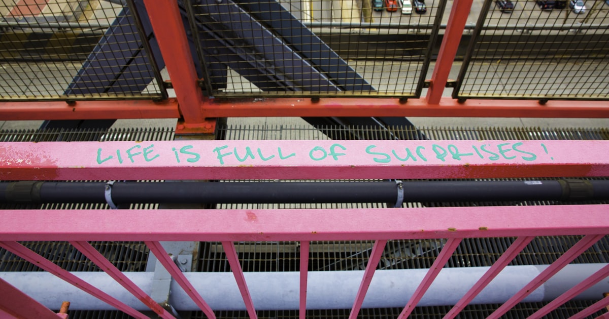 Pink metal structure with 'life is full of surprises' text.