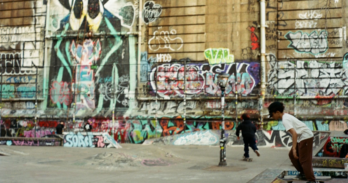 People skateboarding in a gritty urban skatepark with colorful graffiti.