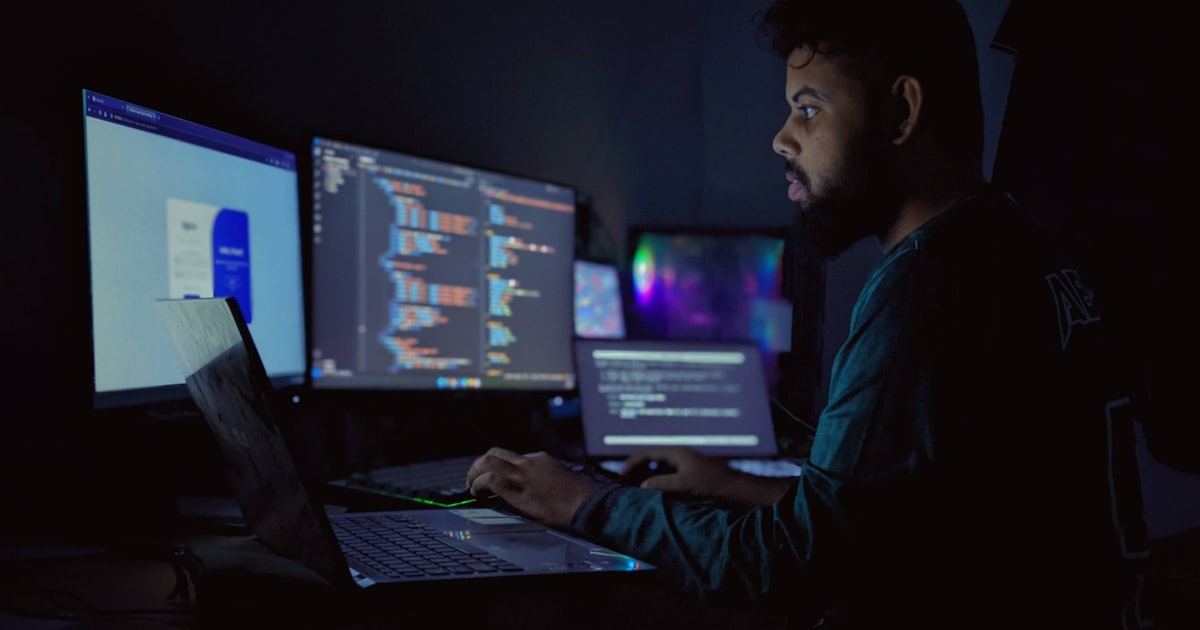 A man sitting in front of three computer monitors