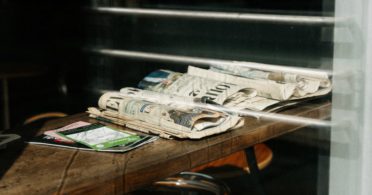 Stack of newspapers and magazines on a wooden table.