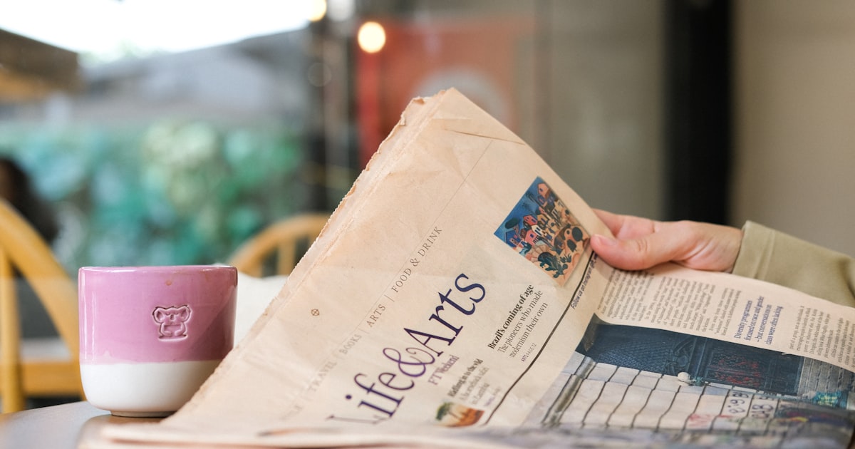Someone is reading a newspaper with coffee.