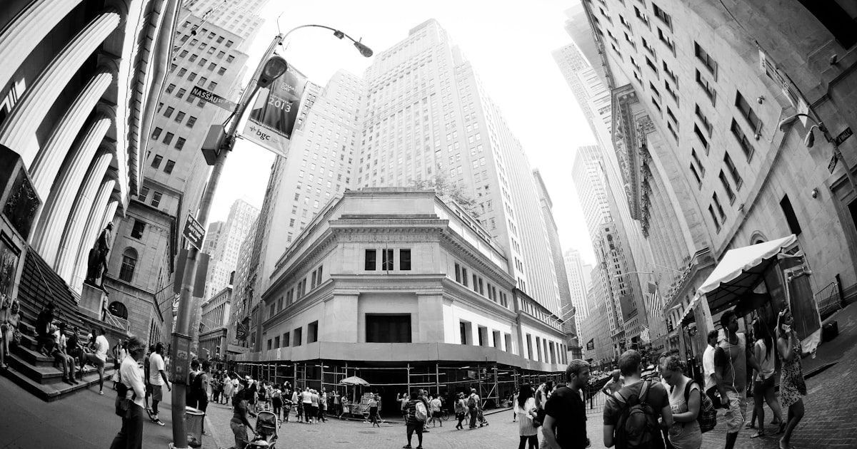 People walk through a bustling city street with tall buildings.