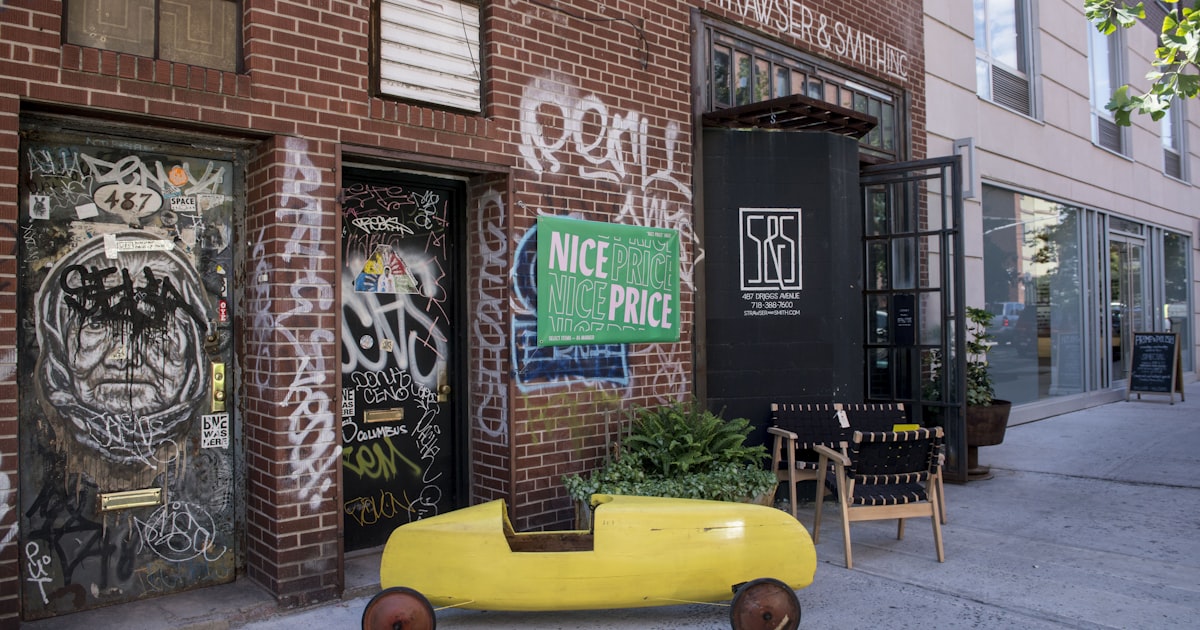 Yellow wooden car outside a graffiti-covered brick building.