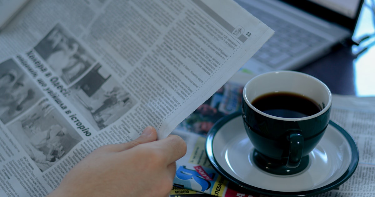 a person reading a newspaper with a cup of coffee
