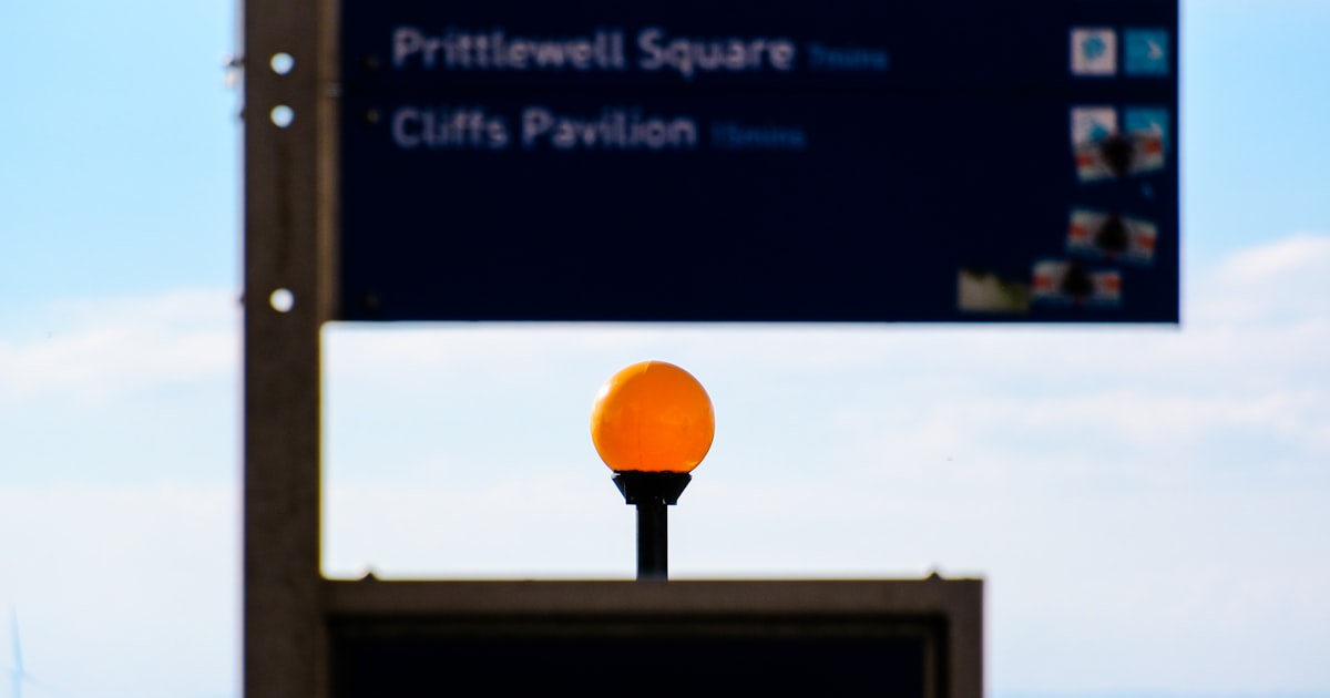 A street sign with an orange ball on top of it